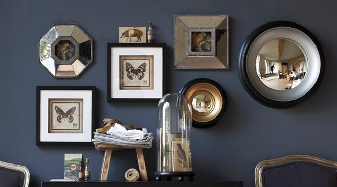 Cabinet de curiosités : papillons encadrés, miroirs anciens et cloche en verre sur un mur bleu nuit