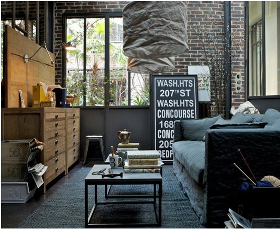 Salon de style industriel : murs de briques, verrière d’atelier, meuble de métier en bois et canapé gris