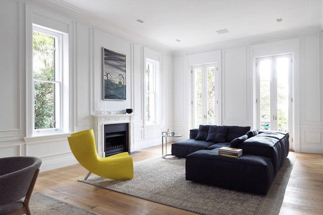 Salon minimaliste : murs blancs, canapé noir, fauteuil jaune et parquet clair