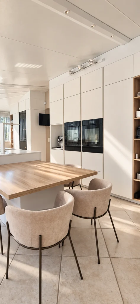 Cuisine blanche haut de gamme avec colonnes four encastrées et table de repas en bois clair